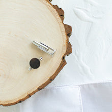 Load image into Gallery viewer, Two silver tone brass cufflinks are resting on a wooden display prop, against a white textured background.