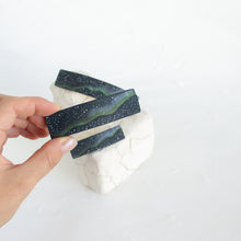 Load image into Gallery viewer, A hand holds up a medium size dark blue polymer clay barrette with a northern lights design, against a white background.
