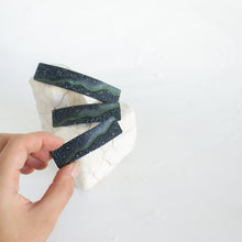 Load image into Gallery viewer, A hand holds up a small size dark blue polymer clay barrette with a northern lights design, against a white background.