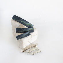 Load image into Gallery viewer, Three dark blue polymer clay barrettes with a northern lights design are arranged on a white rock against a white background.