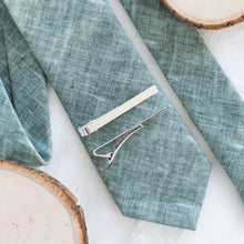Load image into Gallery viewer, Two silver-tone brass tie clips are styled on a sage green tie with a white background and wooden display props.