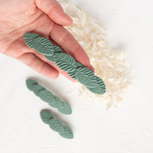 Load image into Gallery viewer, Hand holds a large olive green leaf textured polymer clay hair barrette.