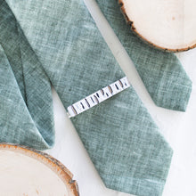 Load image into Gallery viewer, A birch bark pattern brass tie clip is styled with a sage green tie against a white background with wooden display props.
