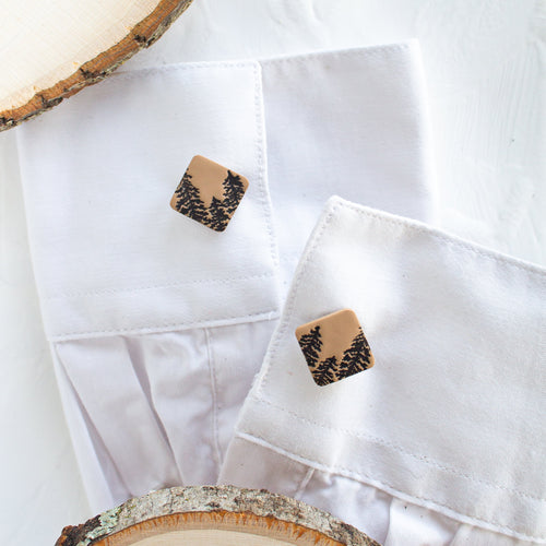 Cufflinks with a brown pine tree pattern are styled on the cuffs of a white shirt, against a white background.
