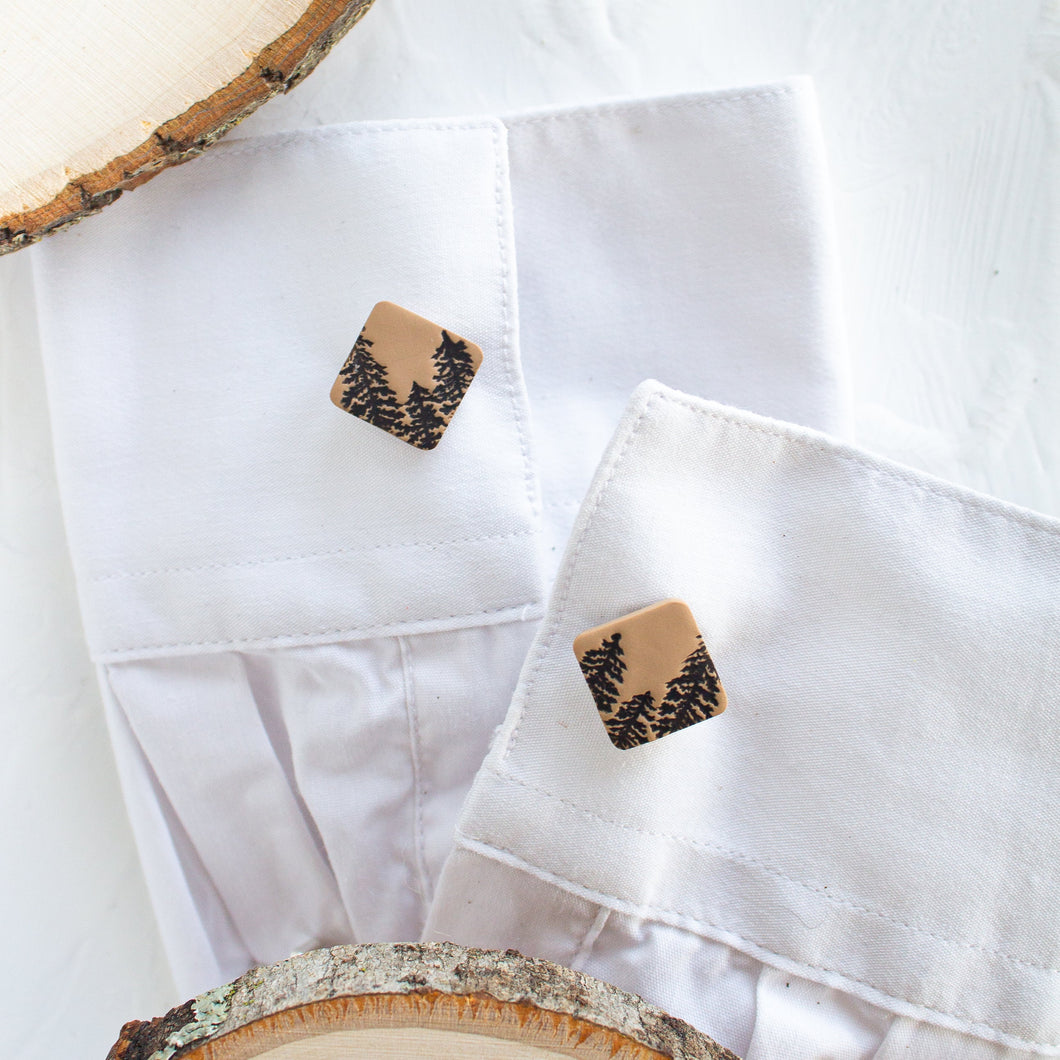 Cufflinks with a brown pine tree pattern are styled on the cuffs of a white shirt, against a white background.