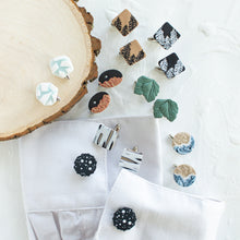 Load image into Gallery viewer, A collection of nature-inspired polymer clay and brass cufflinks are arranged against a white textured background with a wooden display prop and a white cuff shirt.
