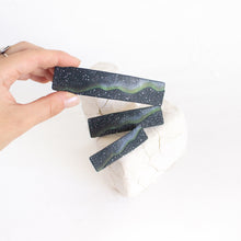 Load image into Gallery viewer, A hand holds up a large size dark blue polymer clay barrette with a northern lights design, against a white background.
