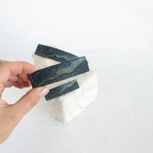 Load image into Gallery viewer, A hand holds up a medium size dark blue polymer clay barrette with a northern lights design, against a white background.

