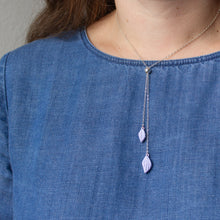 Load image into Gallery viewer, A model with a blue denim shirt wears a silver chain bolo necklace with two lilac purple polymer clay petals on the ends.
