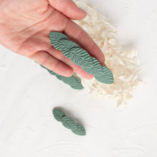 Load image into Gallery viewer, Hand holds a medium olive green leaf textured polymer clay hair barrette.
