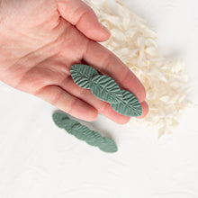 Load image into Gallery viewer, Hand holds a small olive green leaf textured polymer clay hair barrette.
